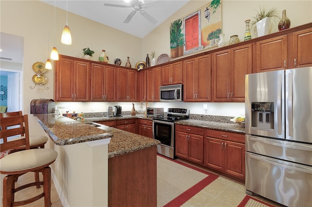 kitchen featuring kitchen peninsula, appliances with stainless steel finishes, dark stone counters, a breakfast bar area, and vaulted ceiling