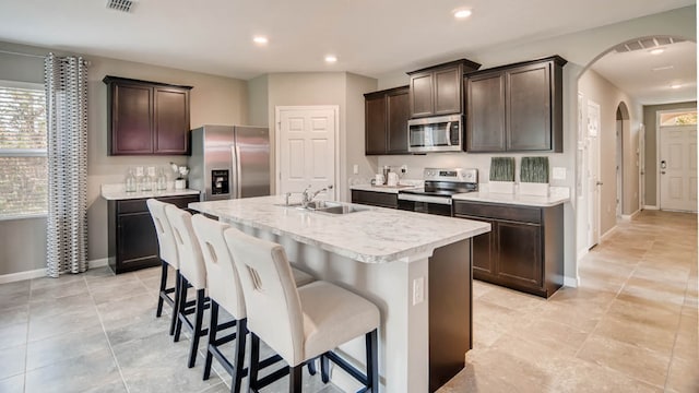 kitchen with dark brown cabinetry, sink, a kitchen bar, a center island with sink, and appliances with stainless steel finishes