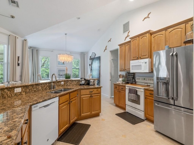 kitchen featuring white appliances, lofted ceiling, decorative light fixtures, dark stone countertops, and sink