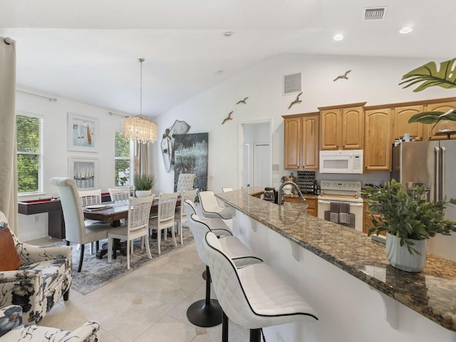 kitchen featuring hanging light fixtures, white appliances, a notable chandelier, dark stone countertops, and lofted ceiling