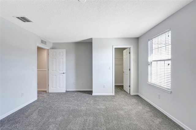 unfurnished bedroom featuring a textured ceiling, carpet floors, a spacious closet, and a closet