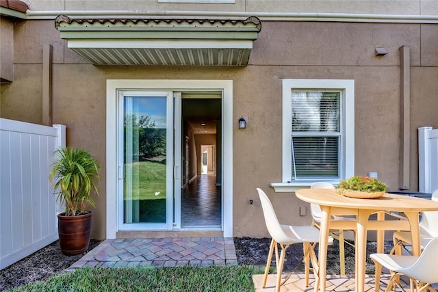 view of exterior entry with fence, a patio, and stucco siding
