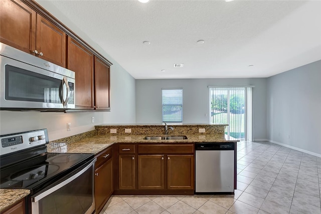 kitchen featuring kitchen peninsula, appliances with stainless steel finishes, stone counters, and sink