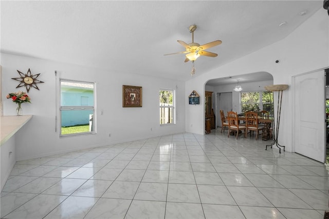 unfurnished living room featuring lofted ceiling, plenty of natural light, light tile patterned flooring, and ceiling fan with notable chandelier