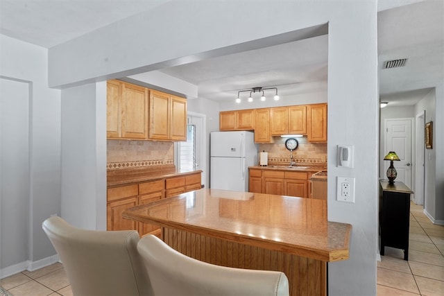 kitchen featuring light brown cabinetry, tasteful backsplash, sink, light tile patterned floors, and white fridge