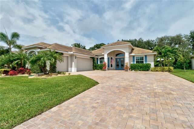 mediterranean / spanish home featuring a garage, french doors, and a front lawn