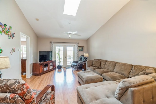 living room featuring french doors, light wood-type flooring, ceiling fan, and vaulted ceiling with skylight