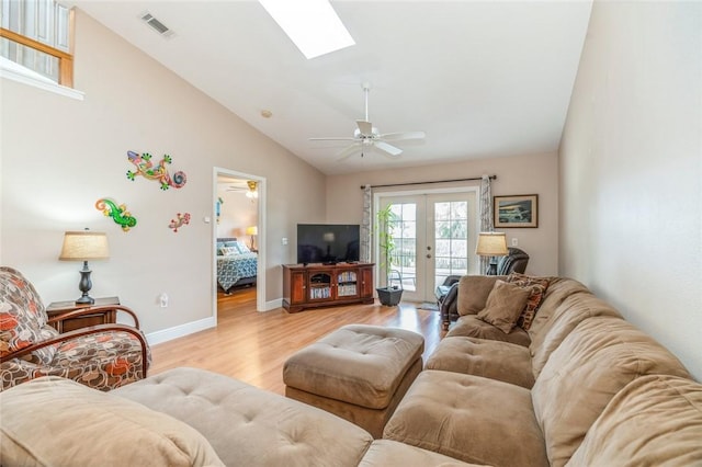 living room featuring vaulted ceiling with skylight, ceiling fan, light hardwood / wood-style floors, and french doors