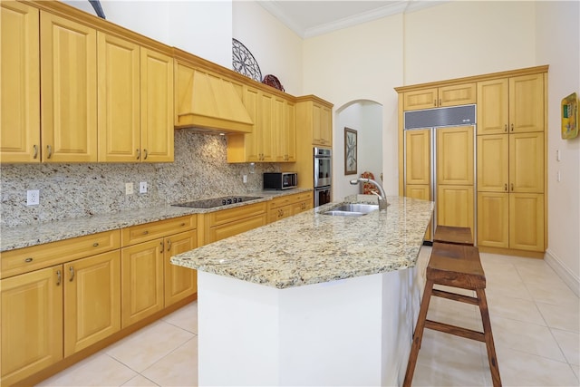 kitchen featuring a towering ceiling, stainless steel appliances, light tile patterned floors, sink, and an island with sink