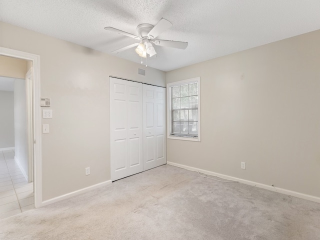 unfurnished bedroom featuring a textured ceiling, light carpet, ceiling fan, and a closet