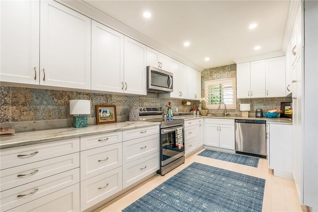 kitchen with white cabinetry, light stone countertops, appliances with stainless steel finishes, and a sink