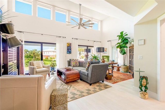 living area featuring a high ceiling, wood finished floors, baseboards, and ceiling fan