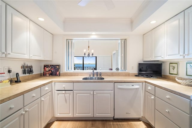 kitchen with a sink, a tray ceiling, white cabinetry, white dishwasher, and crown molding