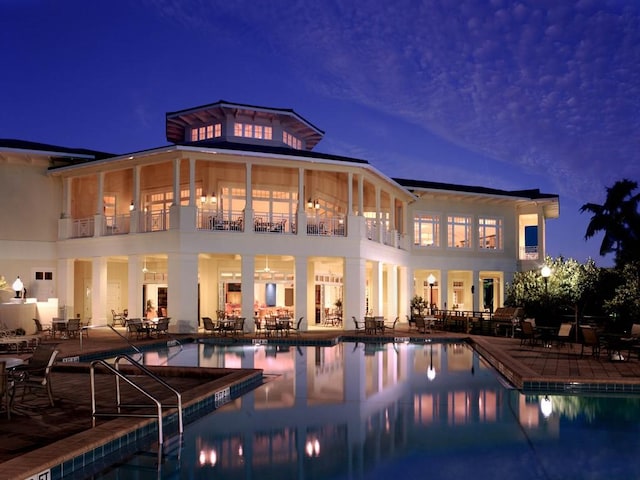 back of house at night featuring a patio area, a balcony, and a community pool