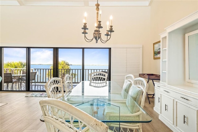 dining area featuring a water view, light wood-style floors, an inviting chandelier, and a towering ceiling