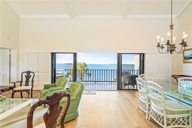 living room with a water view, beam ceiling, light wood-style flooring, a high ceiling, and a notable chandelier