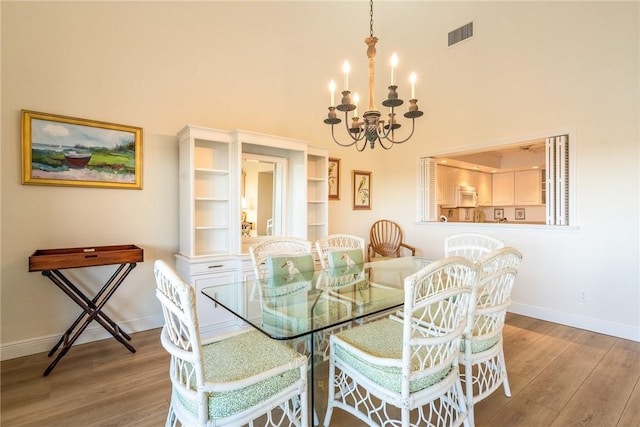 dining space featuring visible vents, wood finished floors, a high ceiling, an inviting chandelier, and baseboards