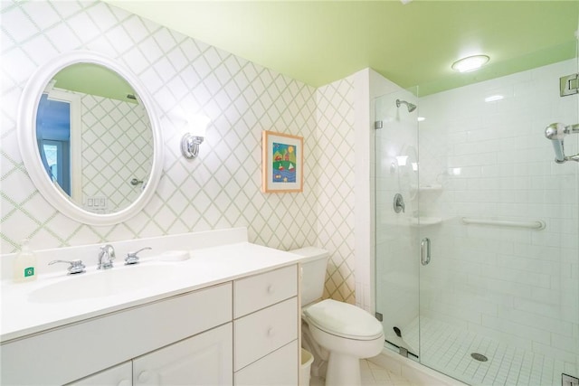 bathroom featuring wallpapered walls, a shower stall, toilet, and vanity