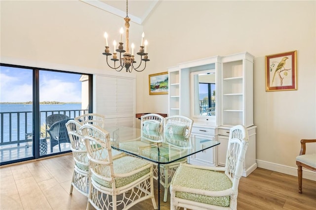 dining space with baseboards, a water view, an inviting chandelier, light wood-style floors, and high vaulted ceiling