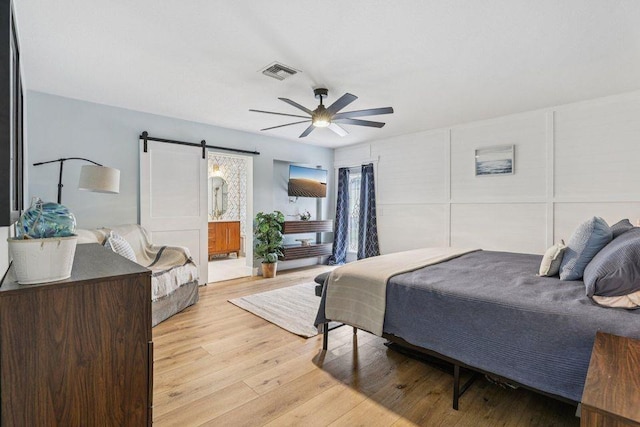 9830 Oak Trl, Sebastian, FL 32976 - bedroom with a barn door, light wood finished floors, ceiling fan, and connected bathroom
