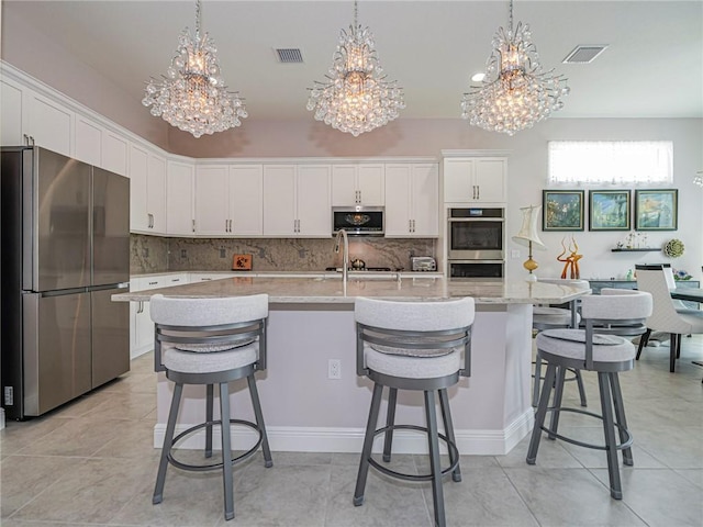 kitchen with decorative light fixtures, an island with sink, white cabinets, and appliances with stainless steel finishes