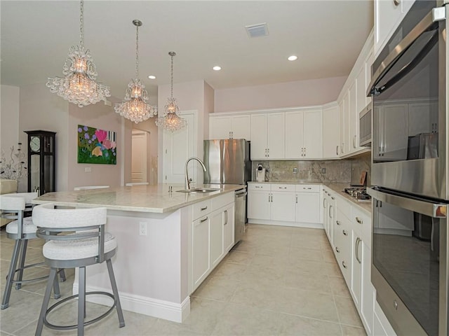 kitchen featuring pendant lighting, appliances with stainless steel finishes, a center island with sink, and white cabinets