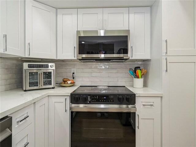 kitchen featuring light stone countertops, decorative backsplash, white cabinetry, and stainless steel appliances