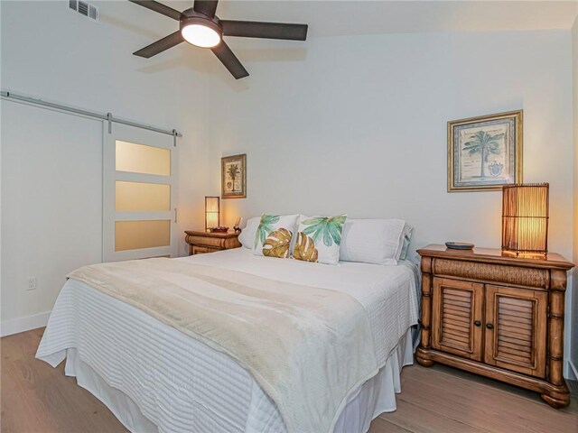 bedroom featuring a barn door, ceiling fan, and light hardwood / wood-style flooring