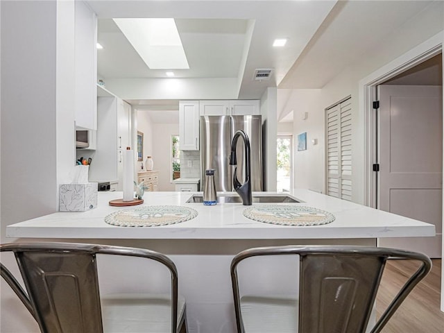 kitchen featuring kitchen peninsula, stainless steel fridge, a skylight, and white cabinetry