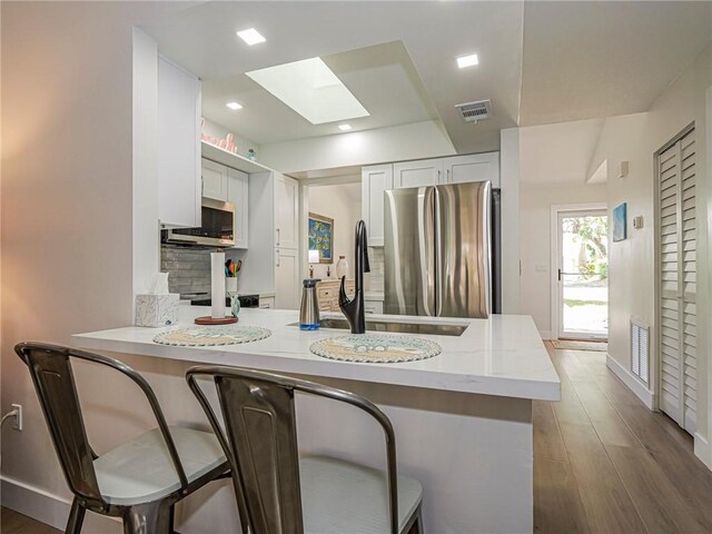 kitchen with a breakfast bar, kitchen peninsula, a skylight, white cabinetry, and stainless steel appliances