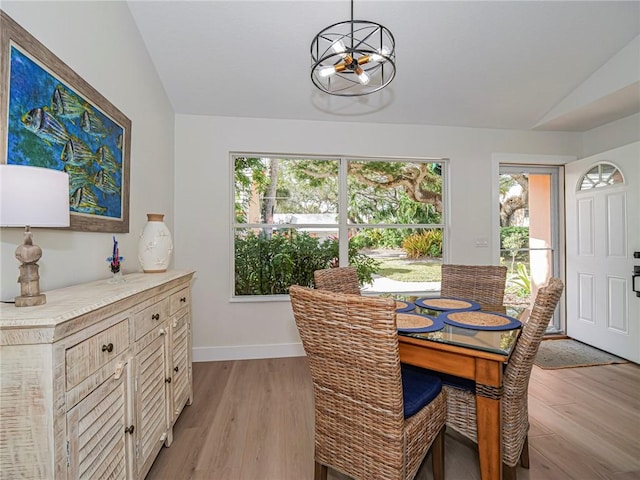 dining room with a notable chandelier, light hardwood / wood-style floors, a wealth of natural light, and vaulted ceiling