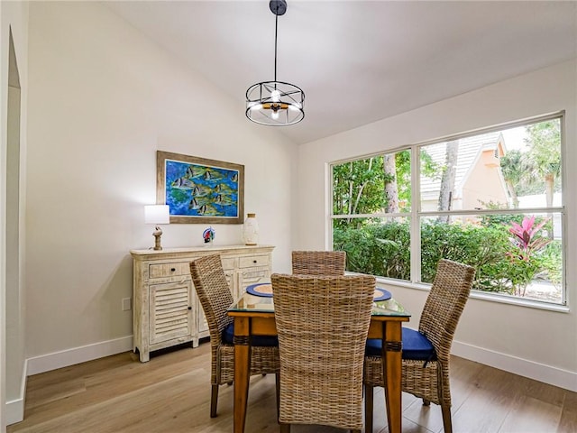 dining area featuring a chandelier, vaulted ceiling, and light wood-type flooring