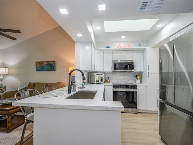 kitchen featuring kitchen peninsula, appliances with stainless steel finishes, backsplash, a breakfast bar, and white cabinetry