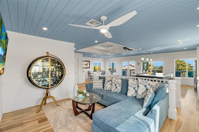 living room featuring ceiling fan, wooden ceiling, a raised ceiling, light hardwood / wood-style flooring, and crown molding