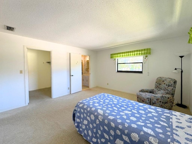 carpeted bedroom with visible vents, a walk in closet, ensuite bathroom, a textured ceiling, and baseboards