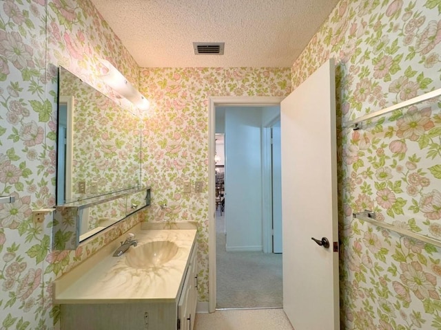 bathroom with visible vents, a textured ceiling, vanity, and wallpapered walls