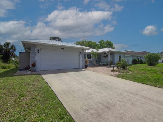 ranch-style home with concrete driveway, an attached garage, a front yard, a standing seam roof, and metal roof