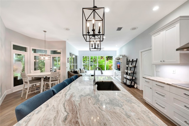 kitchen with light stone counters, a sink, white cabinetry, and decorative light fixtures