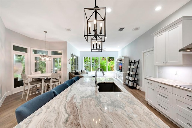 kitchen featuring hanging light fixtures, light stone counters, white cabinets, and a sink