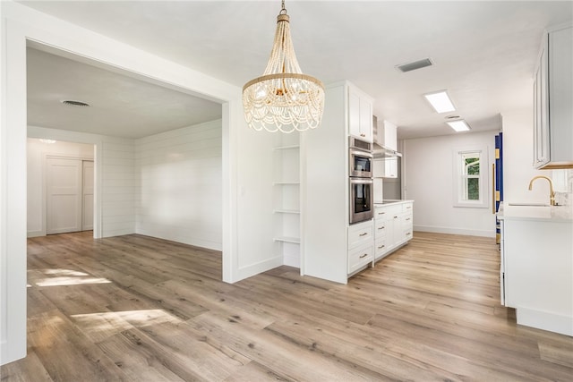 kitchen with white cabinetry, sink, light hardwood / wood-style flooring, and decorative light fixtures