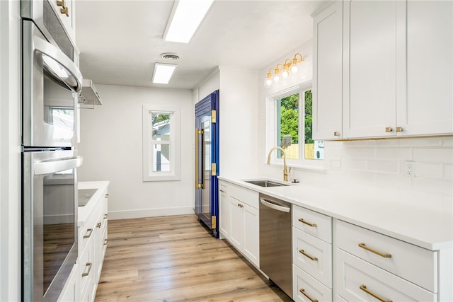 kitchen with light wood-type flooring, appliances with stainless steel finishes, sink, and white cabinets