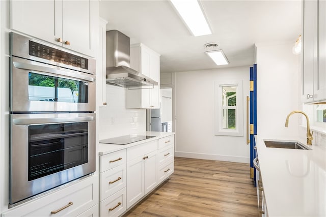 kitchen with white cabinetry, sink, wall chimney range hood, and stainless steel double oven