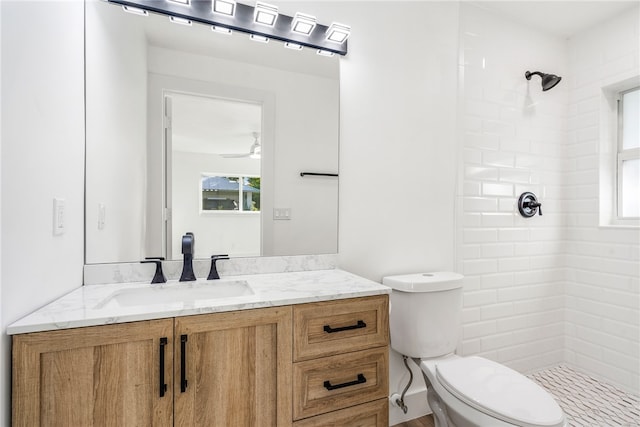 bathroom featuring ceiling fan, vanity, toilet, and a tile shower