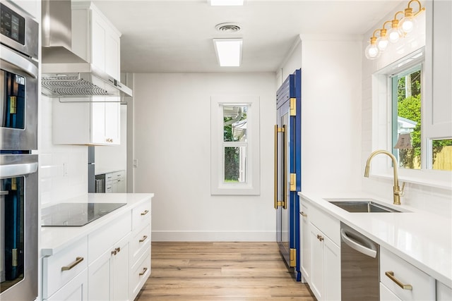 kitchen featuring sink, appliances with stainless steel finishes, wall chimney exhaust hood, light hardwood / wood-style flooring, and white cabinets