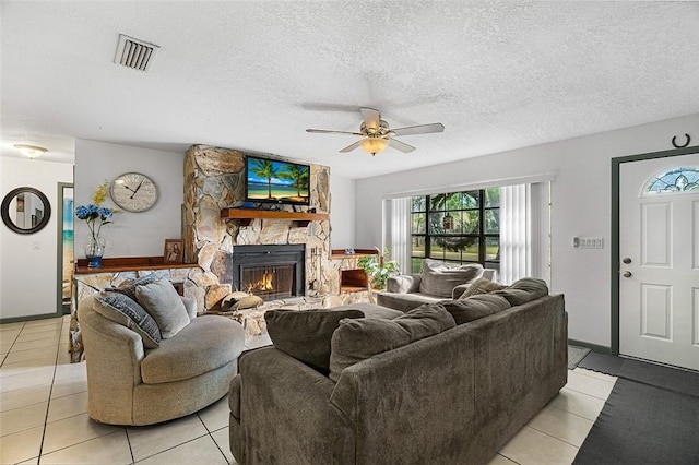 living room featuring a textured ceiling, visible vents, a ceiling fan, and a stone fireplace