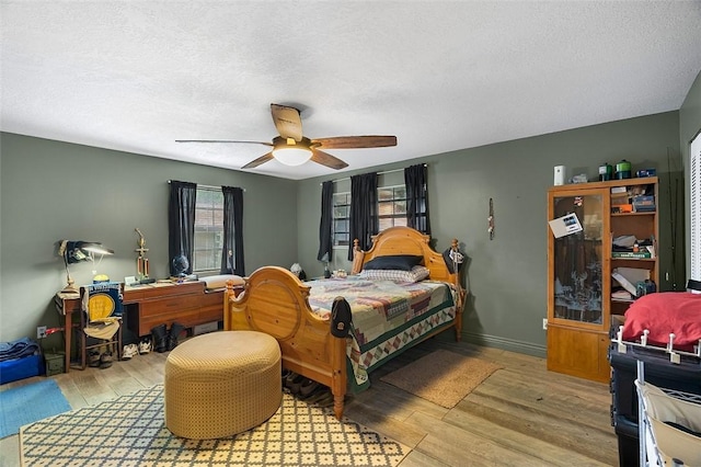 bedroom with ceiling fan, a textured ceiling, baseboards, and wood finished floors