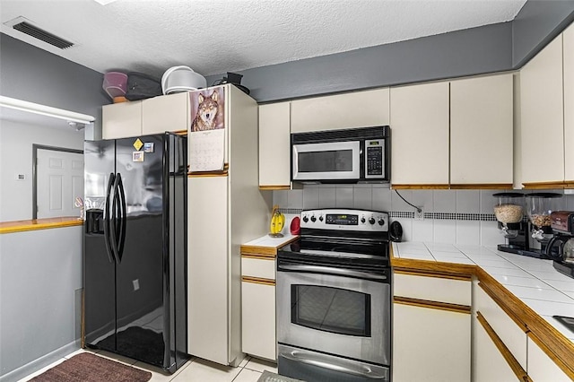 kitchen with tile counters, visible vents, electric stove, white cabinetry, and black fridge