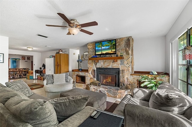 living room featuring a textured ceiling, ceiling fan, a fireplace, and visible vents