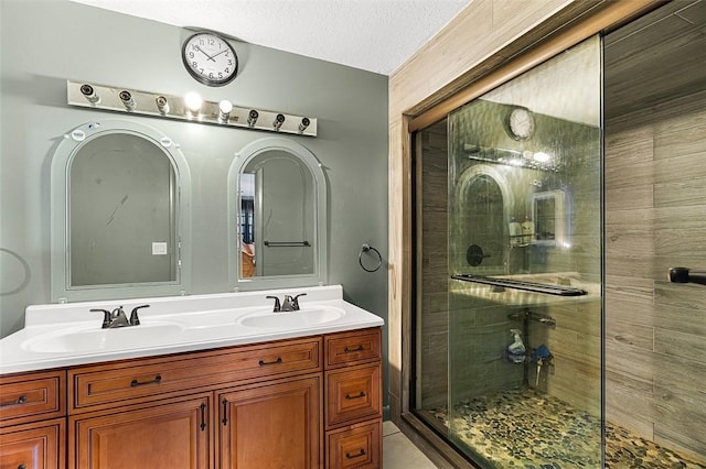 bathroom with double vanity, a stall shower, a textured ceiling, and a sink