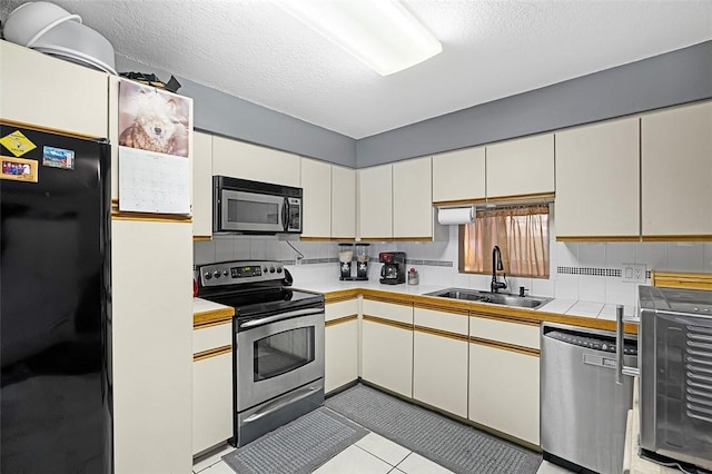 kitchen with a textured ceiling, light tile patterned floors, a sink, appliances with stainless steel finishes, and backsplash